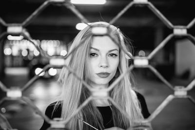 Portrait of young woman standing at parking garage seen through fence