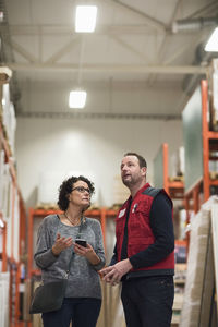 Female customer holding smart phone while talking to salesman in hardware store