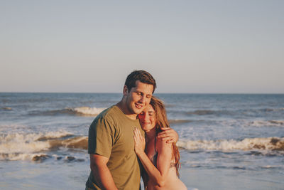 Young couple standing at beach against clear sky