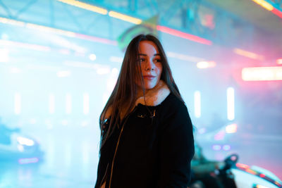 Young woman standing against illuminated wall