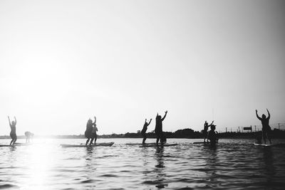 Silhouette people exercising on paddleboard in sea against sky