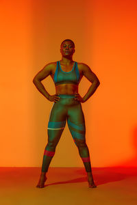 Confident woman with hand on hip standing against orange background