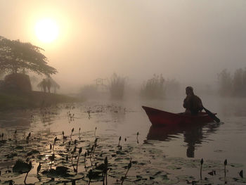 Man sitting on boat moored in lake during sunset