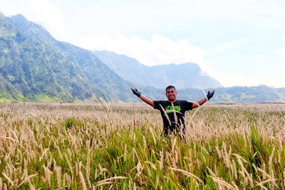 Rear view of man with arms outstretched standing on field against mountain