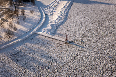 Aerial of a pier extending into an ice and snow covered lake with bare trees along the shoreline.