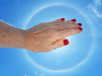 Cropped hand of woman with red painted fingernails against blue sky