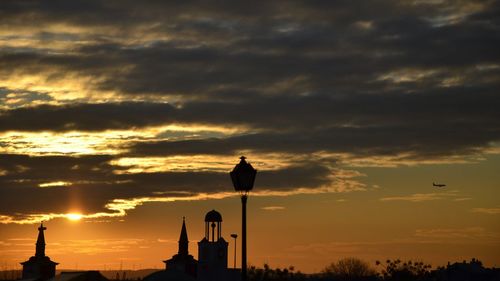 Silhouette buildings against cloudy sky during sunset