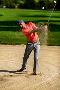 Golfing shot from sand, professional golf player playing from a sand bunker, golf ball in the air