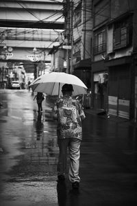 Rear view of man walking with umbrella on wet street