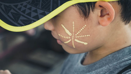 Close-up side view of cute boy with face paint on cheek wearing cap