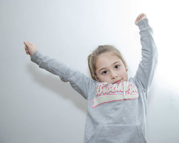 Portrait of girl with arm raised standing against wall