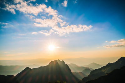 Sunlight streaming through silhouette mountains against sky during sunset