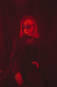 Portrait of young woman wearing sunglasses while standing against black background
