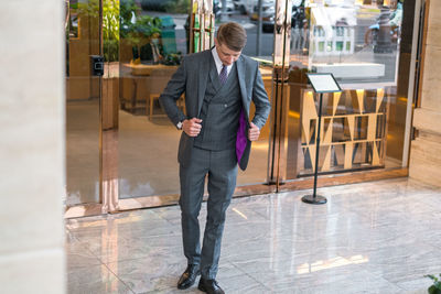 Handsome businessman in grey formal suit standing near modern building and watching down. 