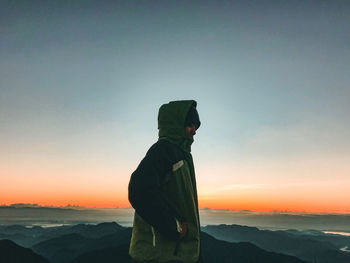 Side view of man standing on rock at sunset