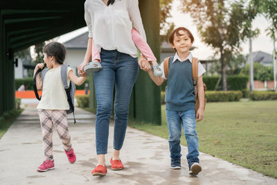 Low section of mother walking with children on footpath during morning