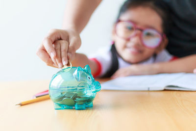 Parent and girl putting coin in piggy bank