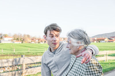 Grandson looking at grandmother on field against clear sky