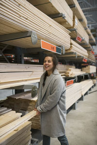 Happy female customer carrying wooden planks by shelves in hardware store