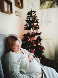 Pregnant woman sitting by christmas tree at home