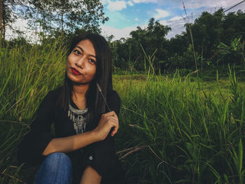 Portrait of beautiful woman sitting on grass against sky