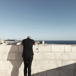 Rear view of man walking on retaining wall against clear sky