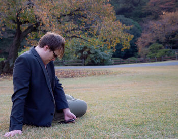Young man looking away while sitting on land