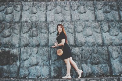 Full length portrait of woman standing against wall