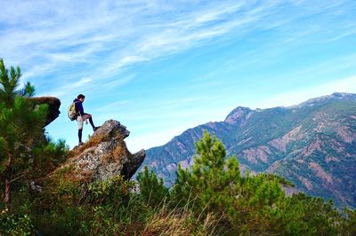Low angle view of person standing on rock against mountain and sky