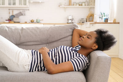 Side view of young woman relaxing on sofa at home