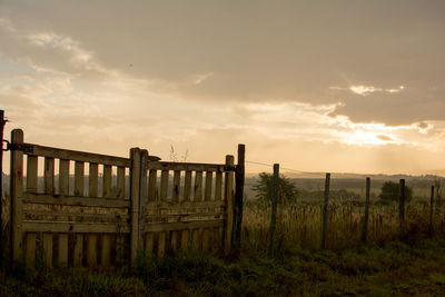 Wooden fence on field against sky during sunset