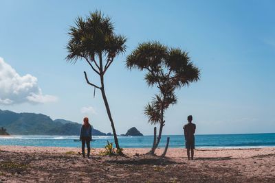Rear view of people standing on beach against sky