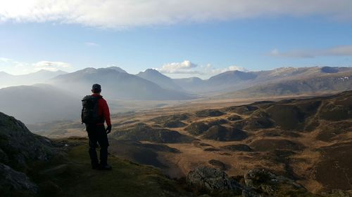 Rear view of hiker standing on field against cloudy sky