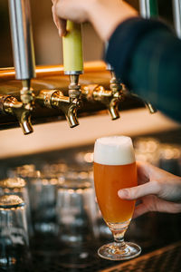 Crop unrecognizable barkeeper pouring foaming beer from tap while working behind counter in pub