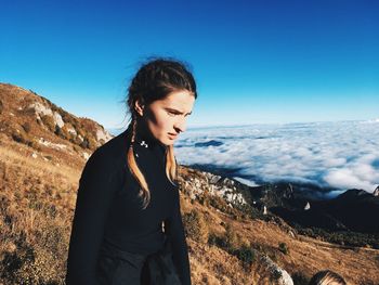 Young woman standing on cliff by cloudscape against clear sky