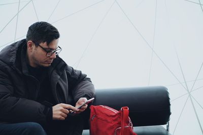 Man using smart phone while sitting on sofa against wall