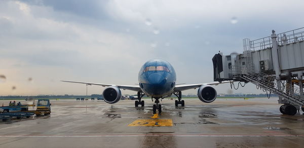 Airplane on wet runway against sky during rainy season