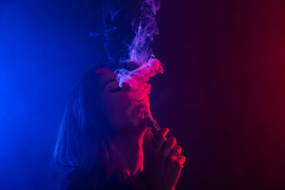 Portrait of young woman smoking over black background