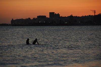 Silhouette people in sea against sky during sunset