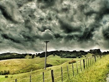 Fence on grassy field against cloudy sky