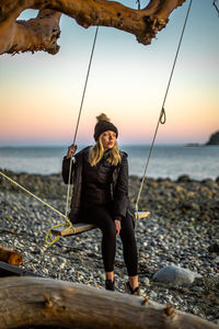 Full length of woman sitting on swing against sea