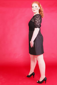 Portrait of young woman standing against red background