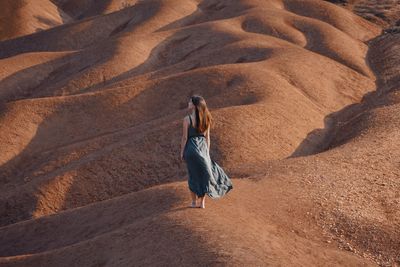 Rear view of woman walking on sand dune in desert