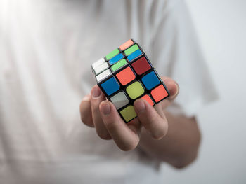 Midsection of man holding puzzle cube while standing against white background