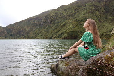 Woman sitting by lake against mountains