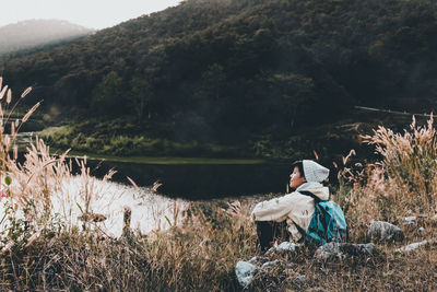 Rear view of man sitting on rock by sea