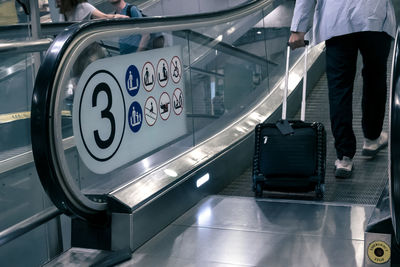 Tourist with travel luggage steps on travelator, tread or moving walkway, emergency stop button