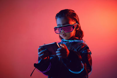 Portrait of robot boy child from the future in neon glasses and jacket looking at the phone at night