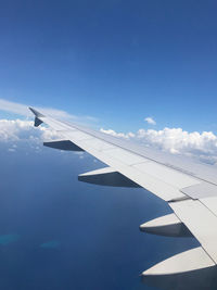 The left wing of an flying airplane in the blue sky. 