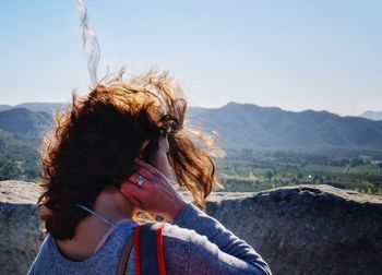 Rear view of woman with tousled hair standing against mountains